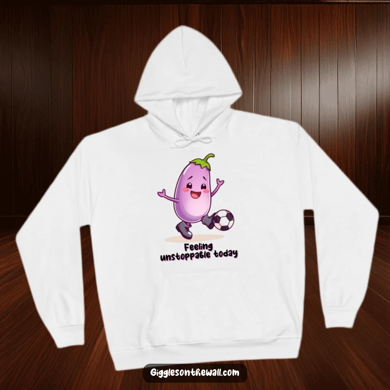Funny hoodie with a smiling eggplant in boots, kicking a football, designed for ultimate comfort and comedic expression.