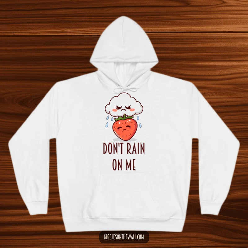 Funny hoodie with a grumpy cloud spitting rain onto a sunbathing strawberry, perfect for staying cozy with a touch of whimsy.