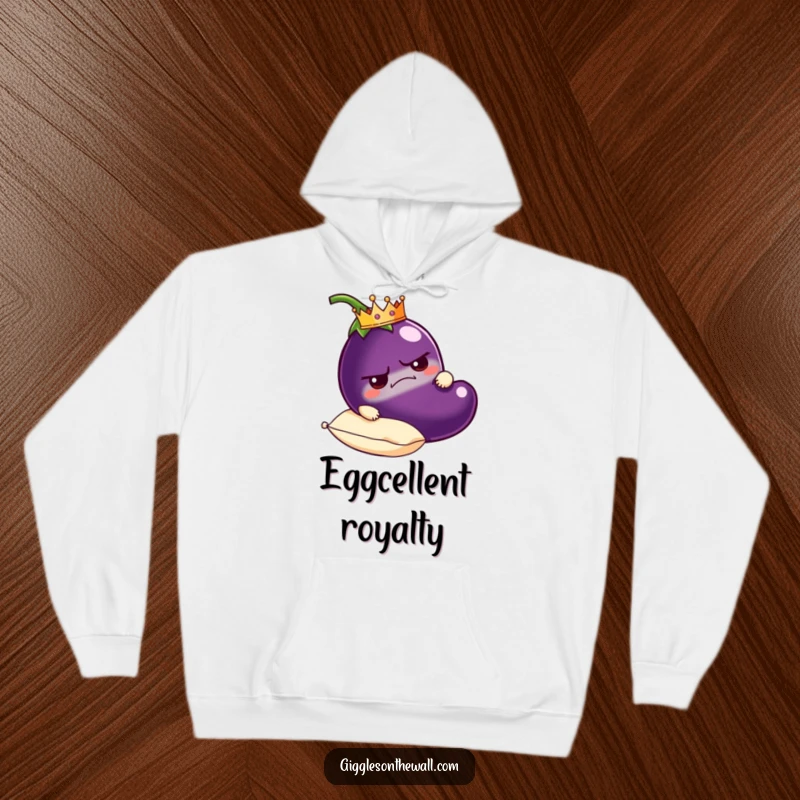 Funny grumpy eggplant hoodie wearing a crown, resting on a plush pillow, cozy and humorous royal apparel.